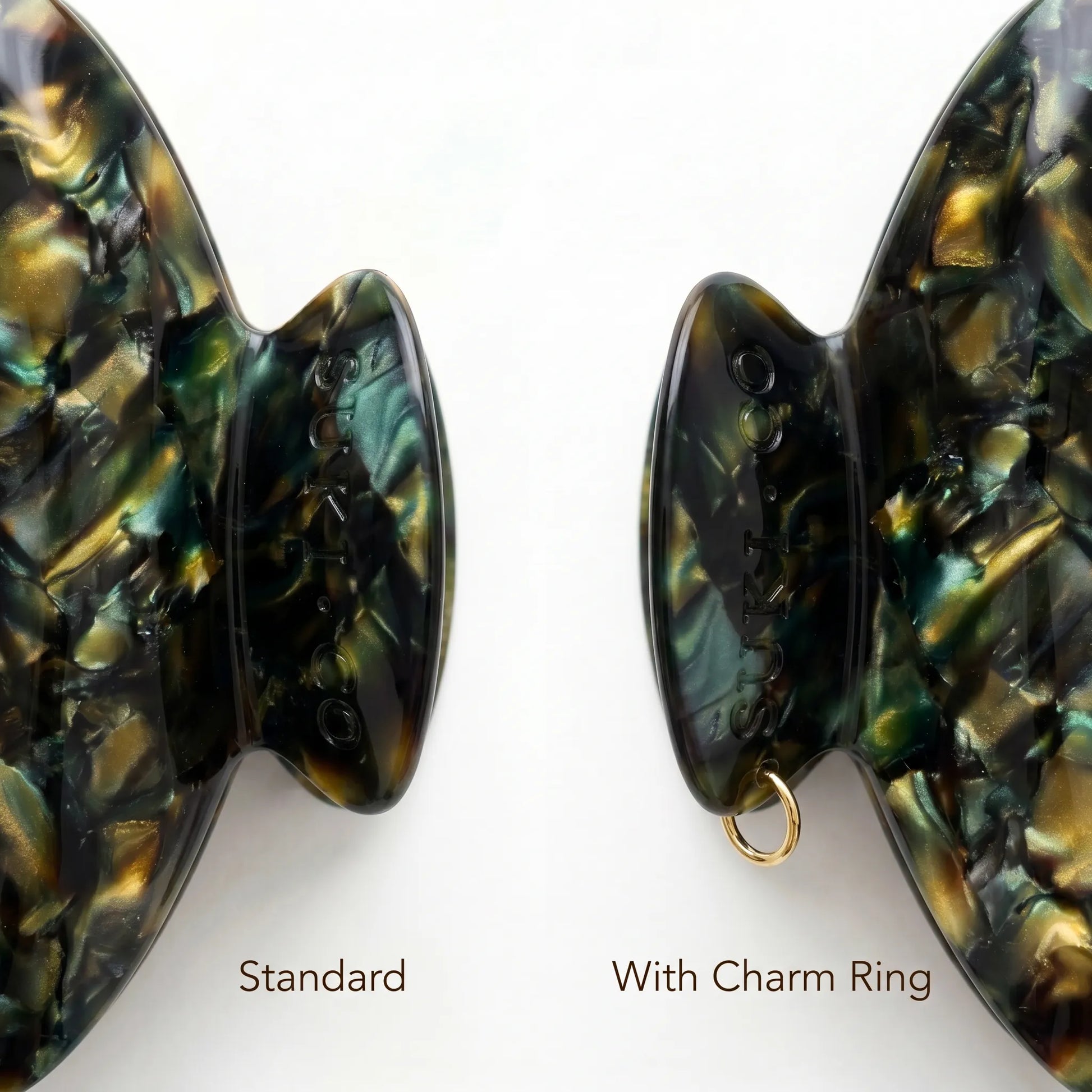Two close-up views of a hair claw clip handle on a white background, labeled 'Standard' and 'With Charm Ring.' The clip has an iridescent abalone shell pattern in black, green, and gold, with a small gold ring shown in the right view.