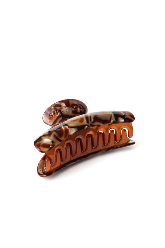 A tortoiseshell hair claw clip with a glossy amber-brown and black marbled pattern and silver shown on a clean white background.