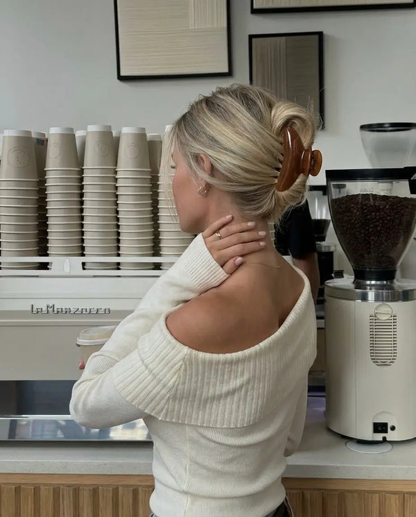 A girl in a coffee shop facing away. Wearing a rich brown claw clip.