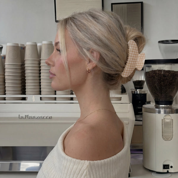 Woman with a hair clip in a coffee shop setting with a La Marzocco machine. Wearing a white and pink gingham checkered claw clip.