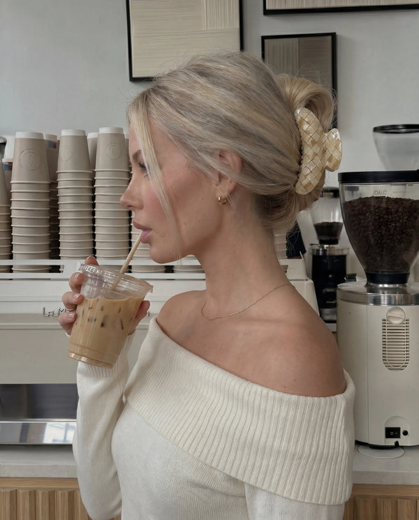 Woman drinking iced coffee in a coffee shop wearing a tiled beige claw clip.