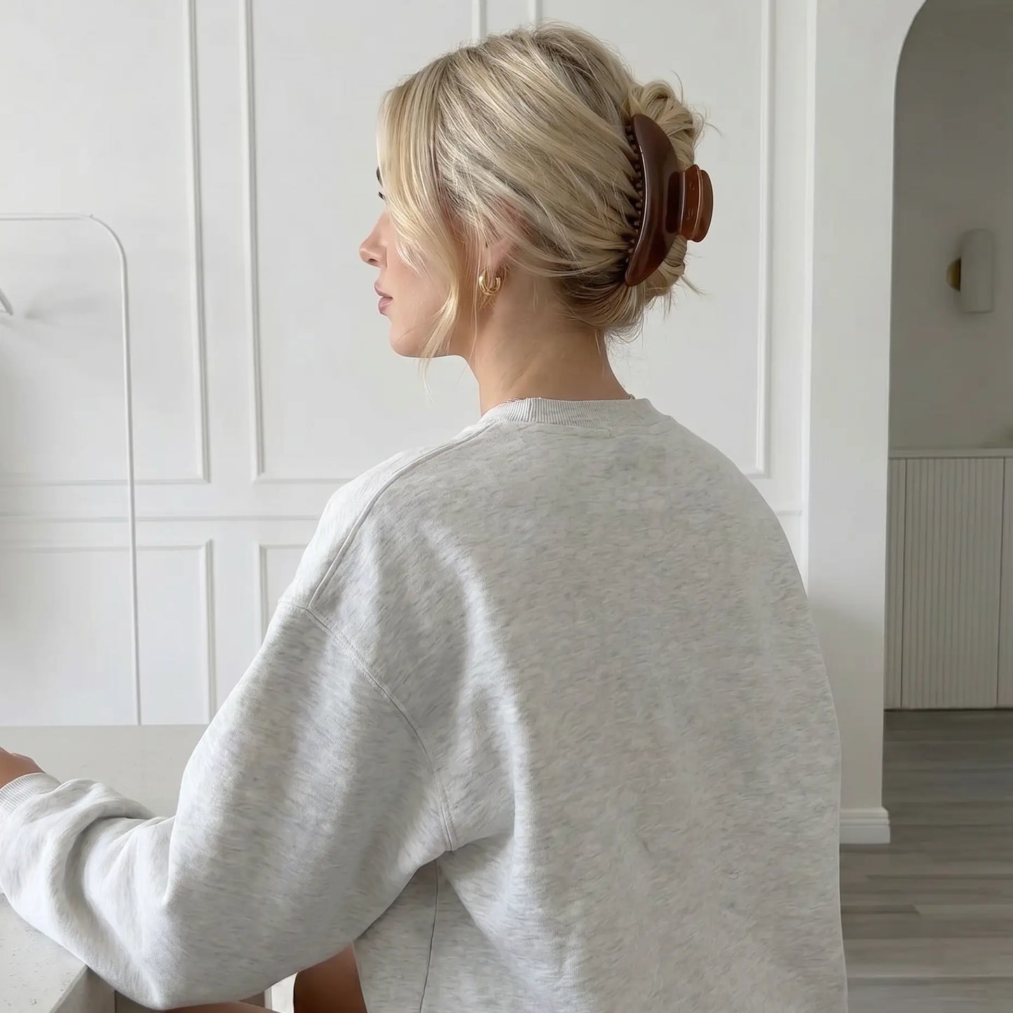 Person wearing a gray sweater in a minimalistic room wearing a slim claw clip that's a rich brown tone.
